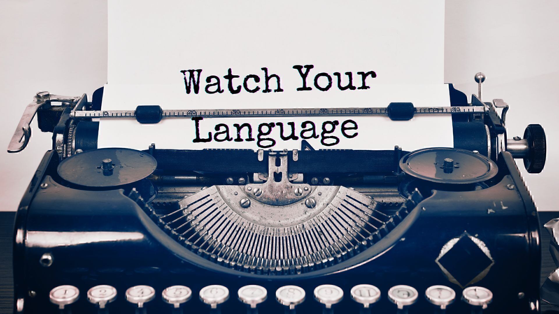 A close up of an old-timey typewriter with the words "Watch your language" typed on the page.