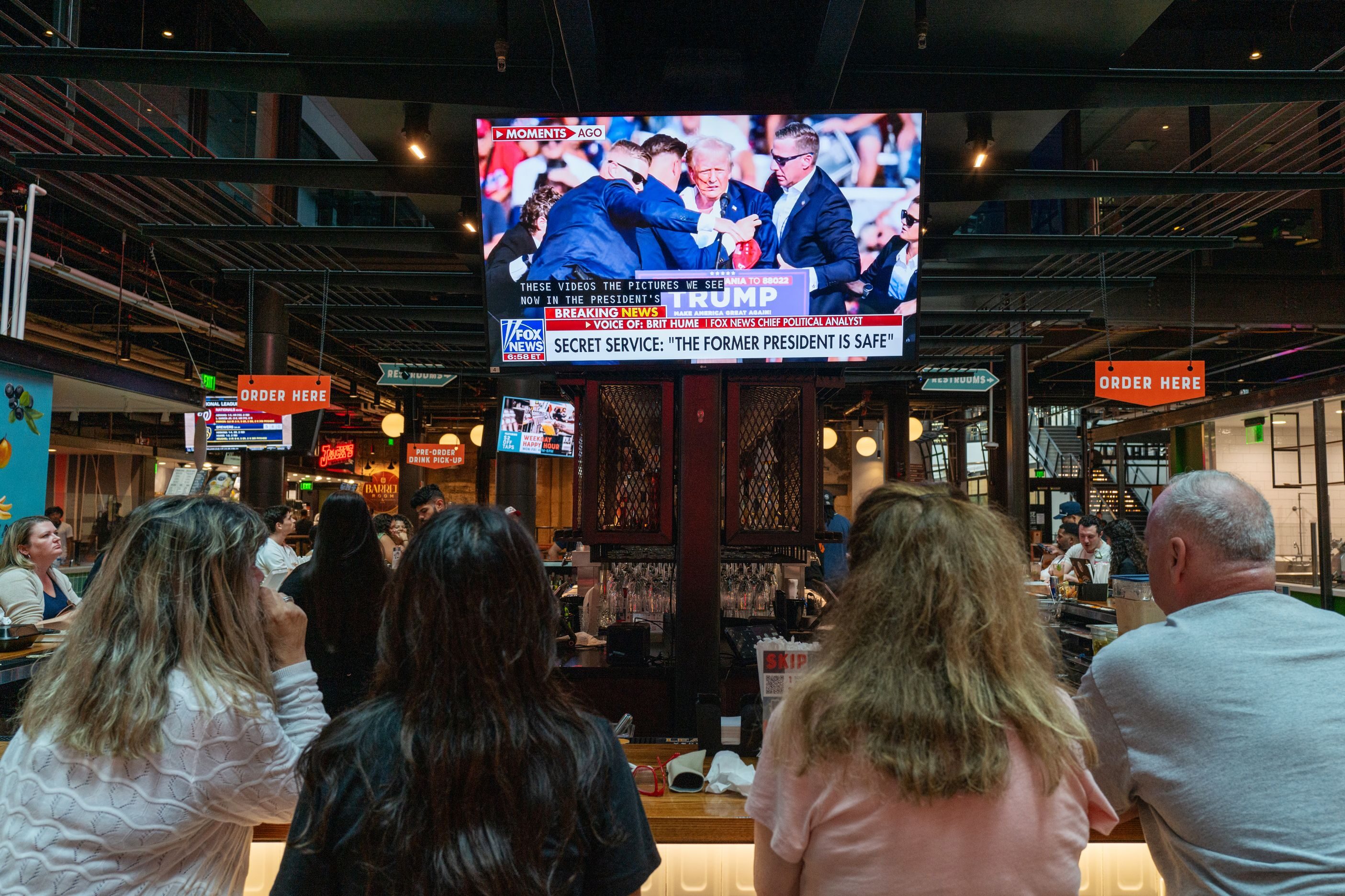 People watch television news at a bar in Milwaukee displaying images from a campaign rally for former U.S. President Donald Trump where he was apparently injured on July 13, 2024 in Milwaukee, Wisconsin. Details are unclear, but Secret Service quickly ushered Trump away while speaking at the Pennsylvania rally.
