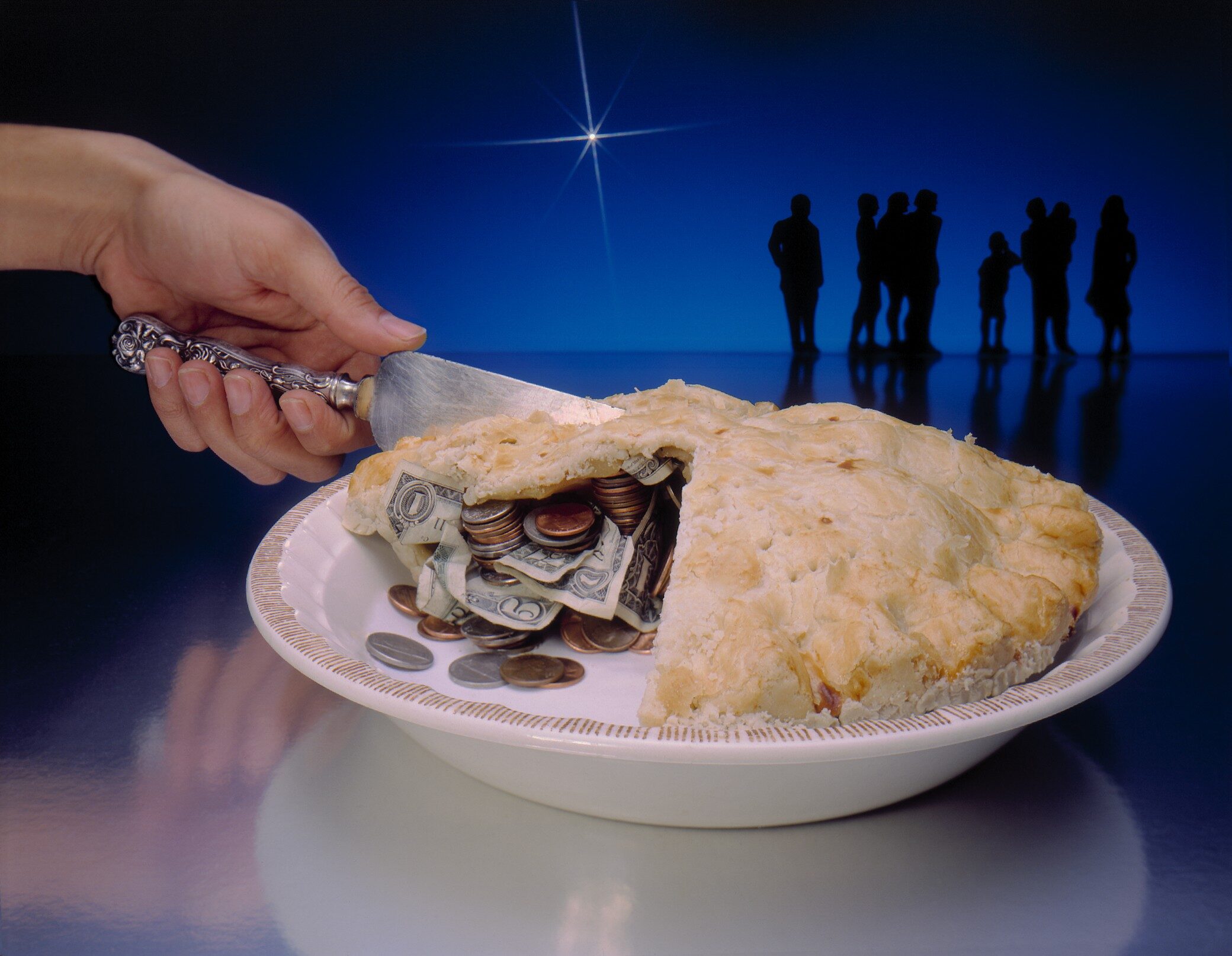 Hand cutting into a baked pie filled with money. There are silhouettes of a group of people standing in the background. The background is blue with a bright cross star.