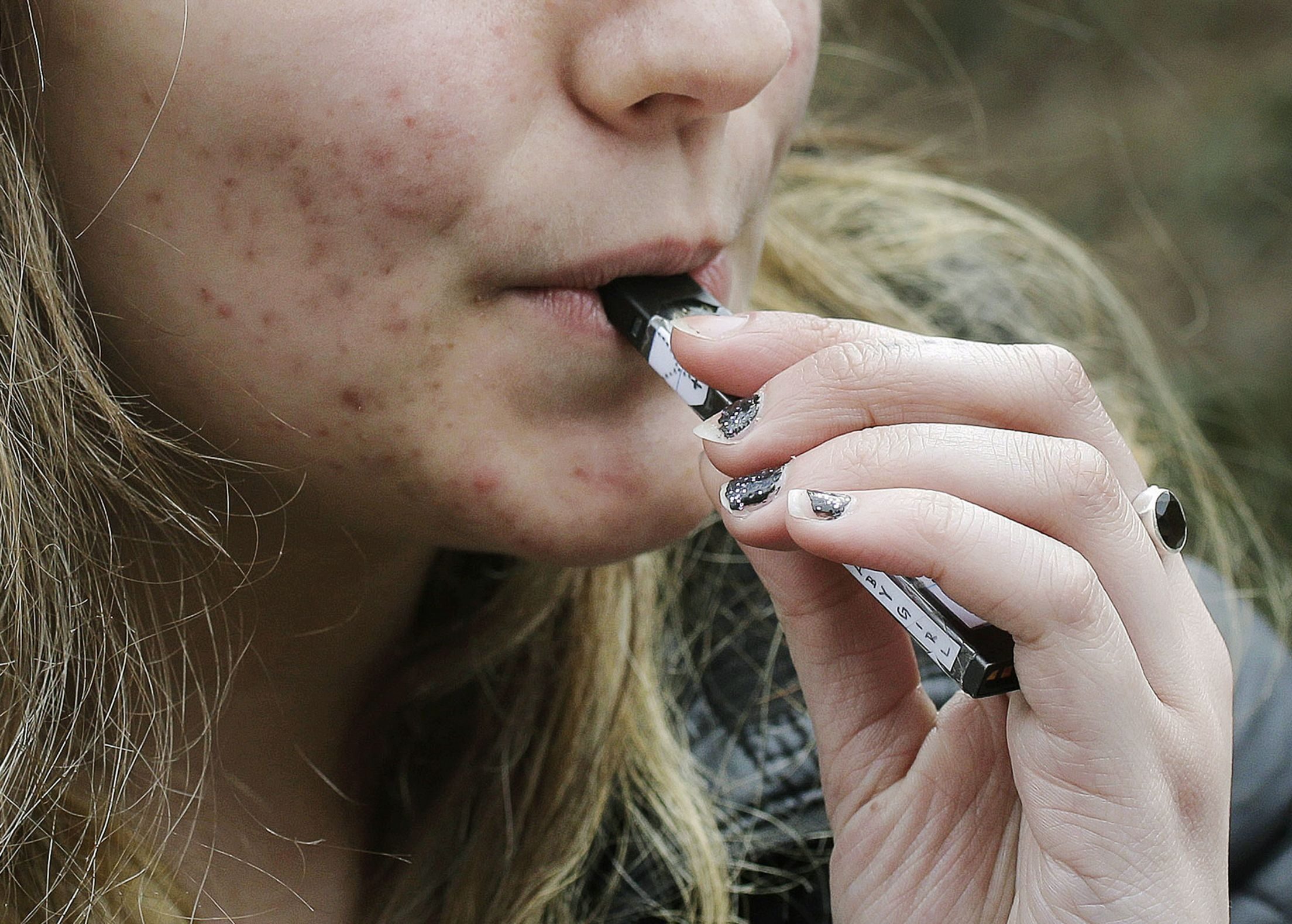 In this April 11, 2018 photo, a high school student uses a vaping device near a school campus in Cambridge, Mass.