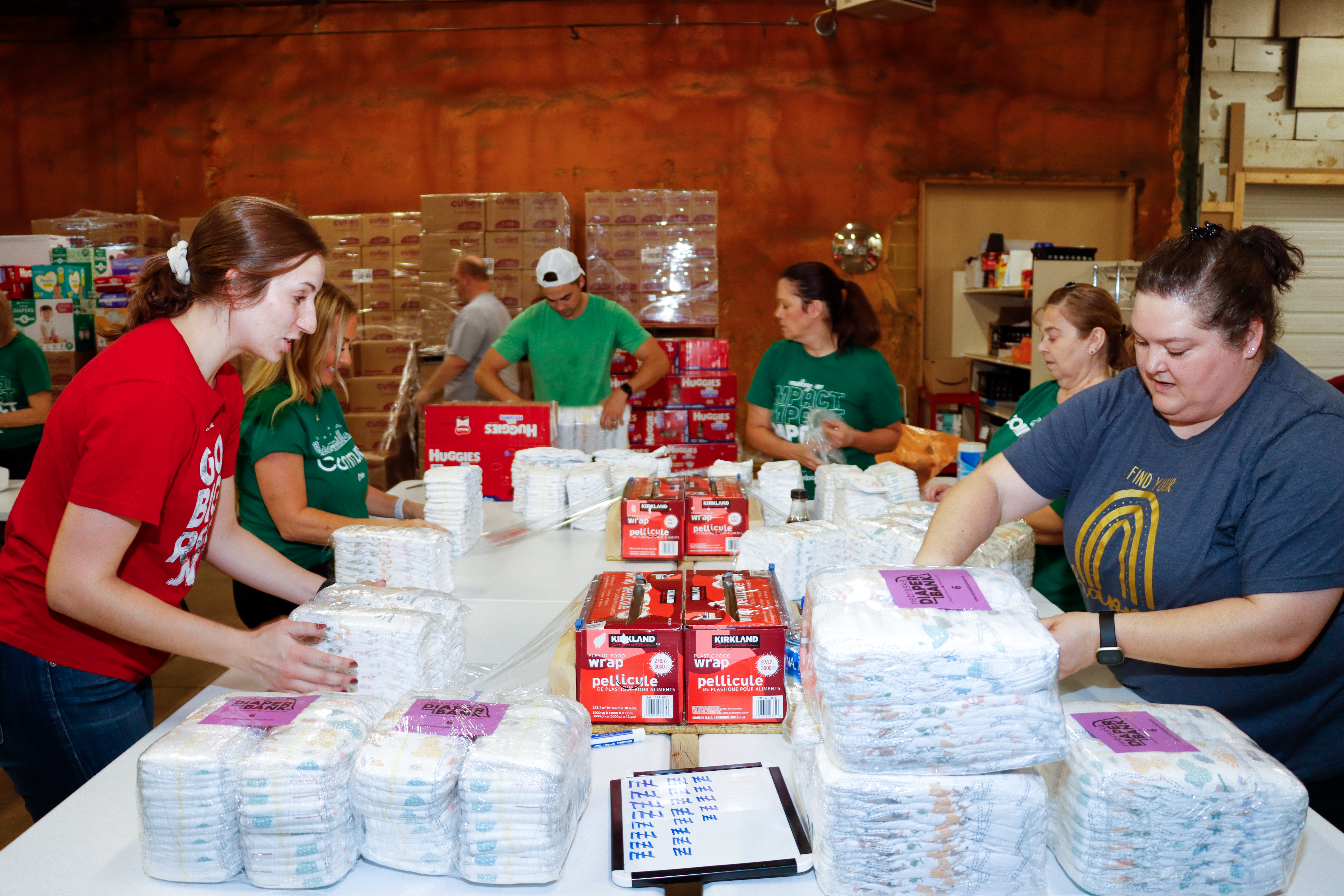 Volunteers appear to work preparing diaper bags with supplies.