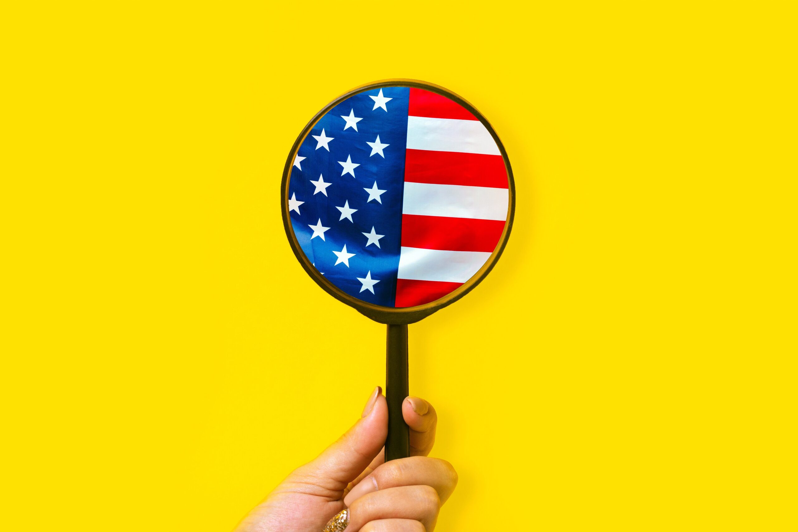 female hand holds a magnifier and looks at the American flag