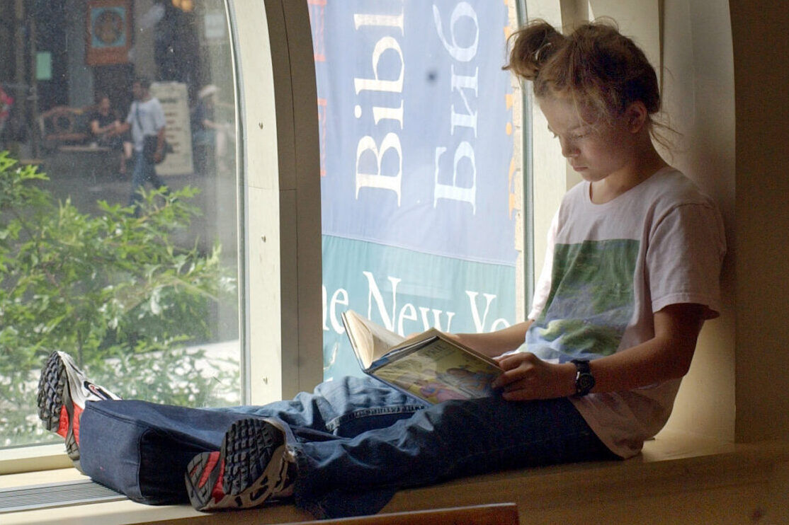 FILE - A young girl reads a book while sitting in a window of the Morningside Heights branch of the New York Public Library on July 29, 2003. (AP Photo/Richard Drew, file)